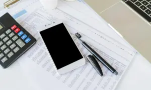 Kalkulator, smartfon, długopis i arkusz kalkulacyjny na biurku.