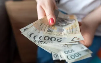 Dłoń trzymająca plik polskich banknotów 200 zł i 100 zł.