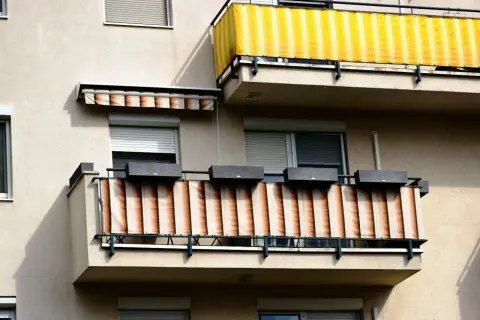 Dwa balkony z osłonami przeciwsłonecznymi: jeden żółto-biały, drugi beżowo-pomarańczowy.