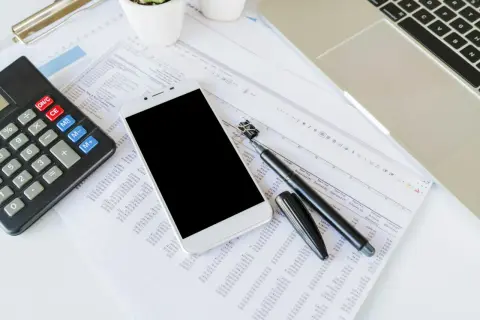 Kalkulator, smartfon, długopis i arkusz kalkulacyjny na biurku.