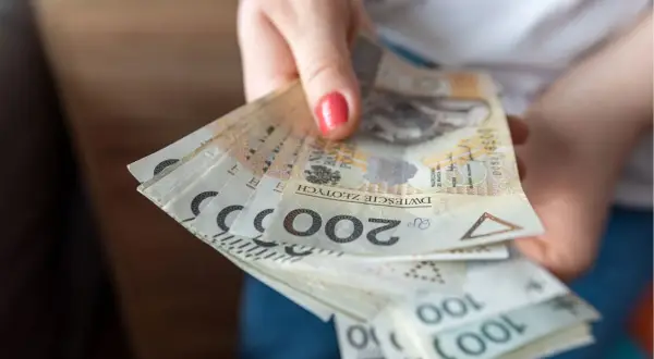 Dłoń trzymająca plik polskich banknotów 200 zł i 100 zł.