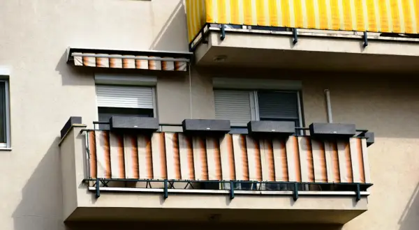 Dwa balkony z osłonami przeciwsłonecznymi: jeden żółto-biały, drugi beżowo-pomarańczowy.