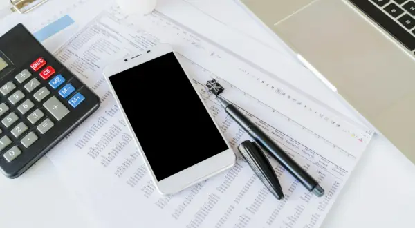 Kalkulator, smartfon, długopis i arkusz kalkulacyjny na biurku.