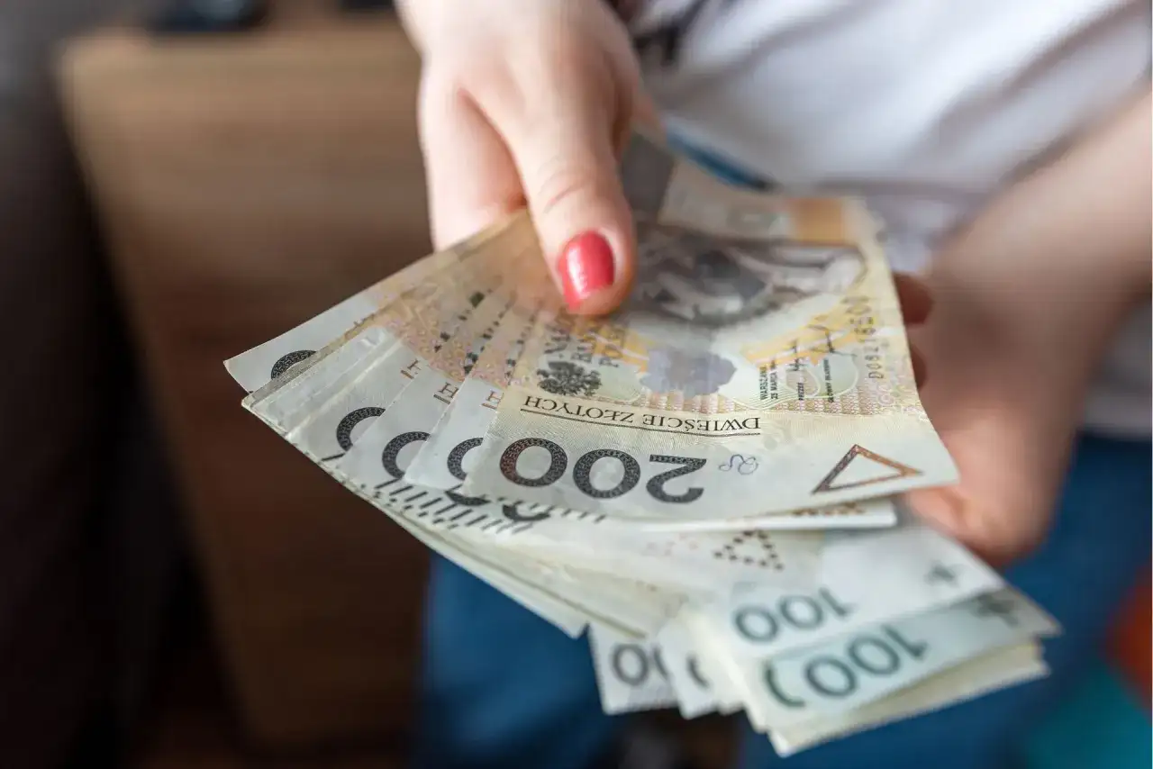 Dłoń trzymająca plik polskich banknotów 200 zł i 100 zł.